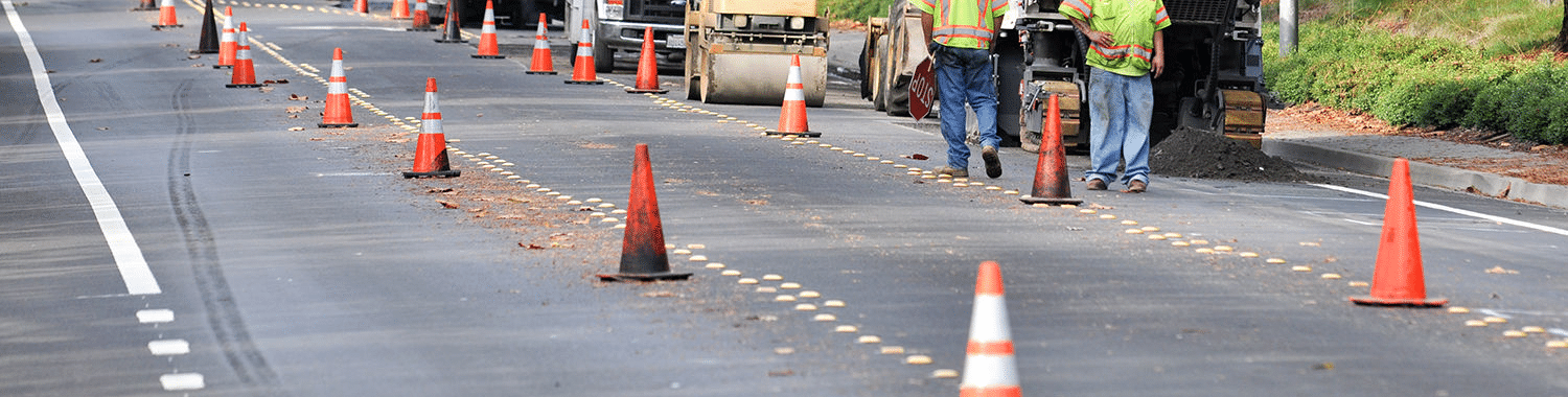 image show road work crew walking on the side of a road with their machines behind them and traffic cones in the road